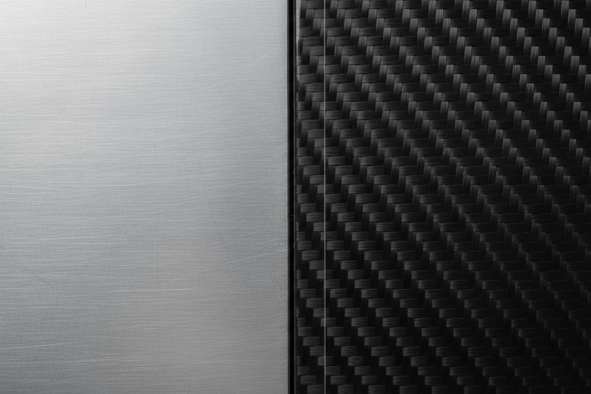 Adjacent flawless aluminum and carbon-fiber aircraft panels meeting at a clean seam under soft light