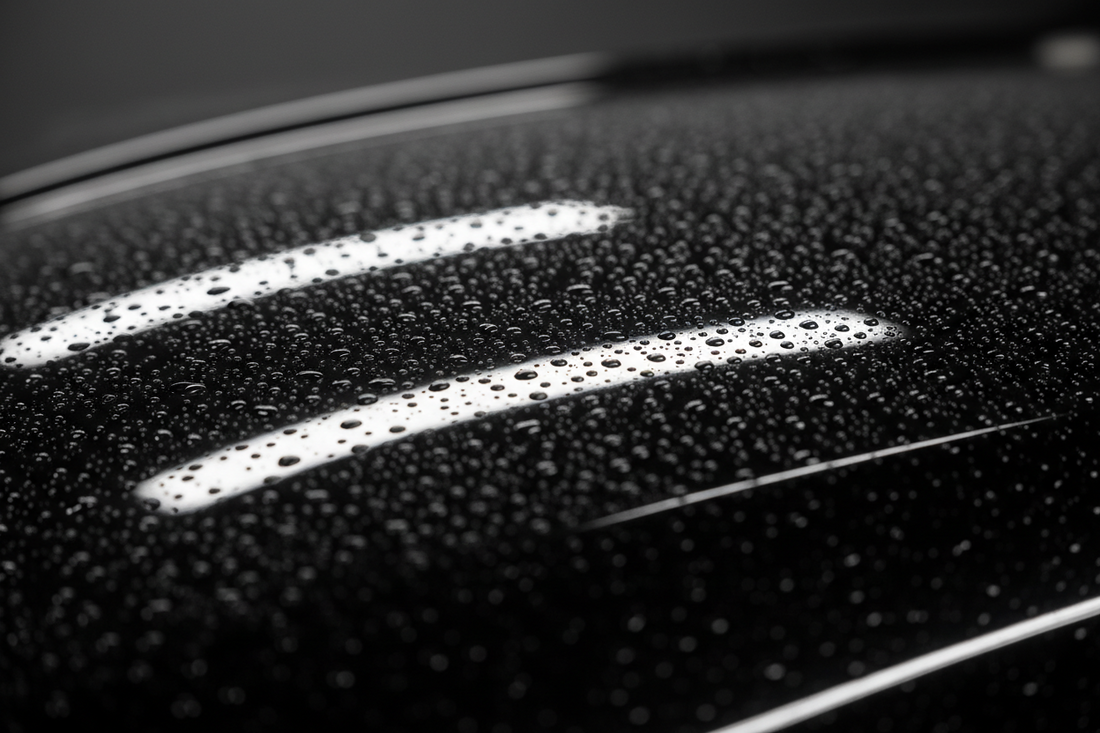 Mirror-gloss black car panel covered in tight uniform water beads